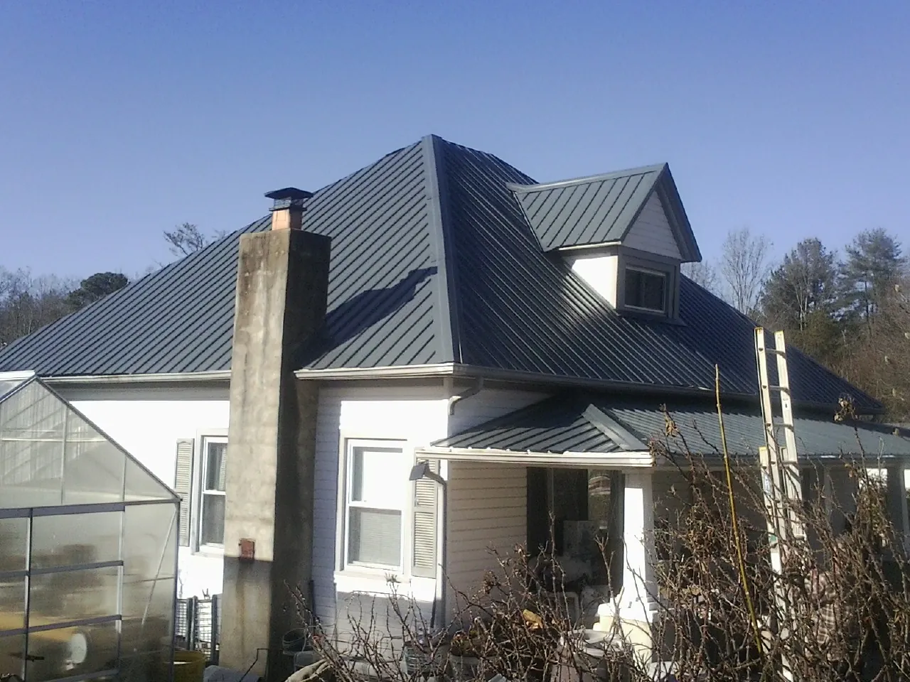 Dark blue standing seam metal roof on a white farmhouse with dormer — Slate & Tile Roof Repair by Roofing Brothers in Huntsville