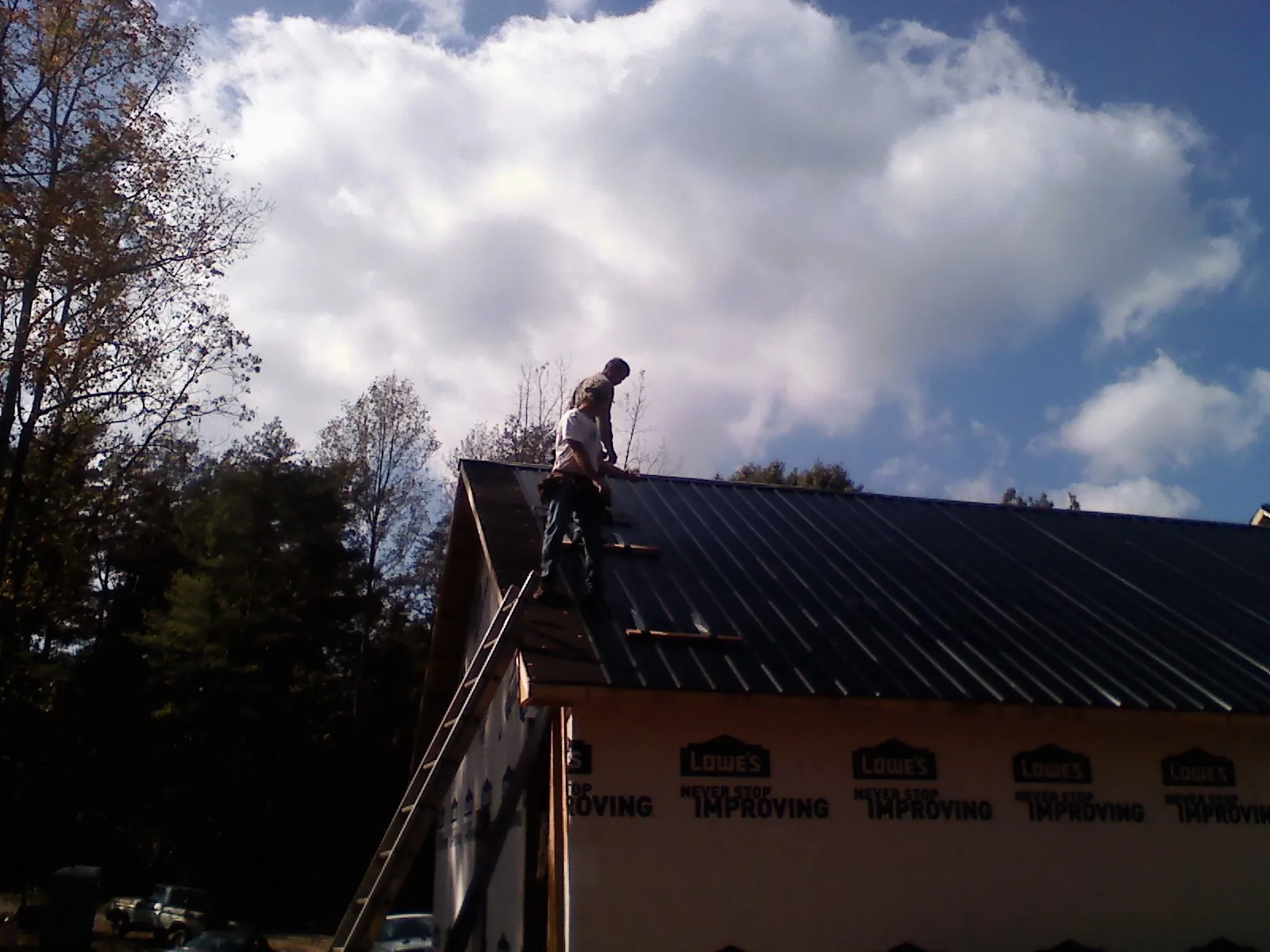 Roofer fastening dark metal panels high against a cloudy sky, from a Roof Inspection job in Huntsville